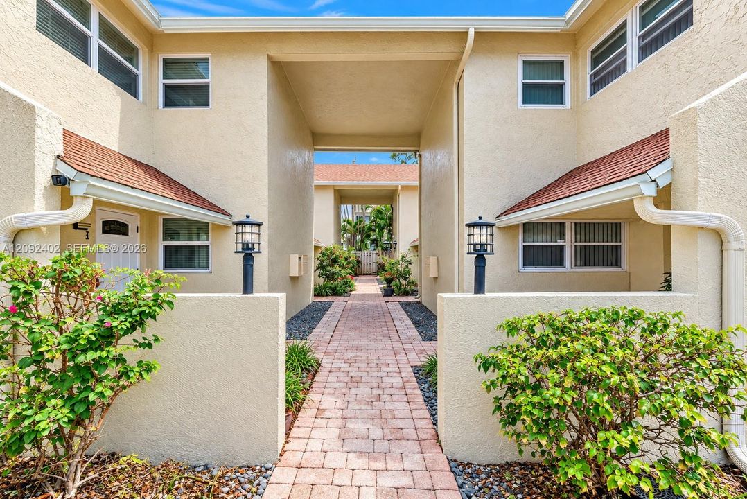 Stucco exterior featuring a paved brick walkway, decorative post lighting, and shingle roofing