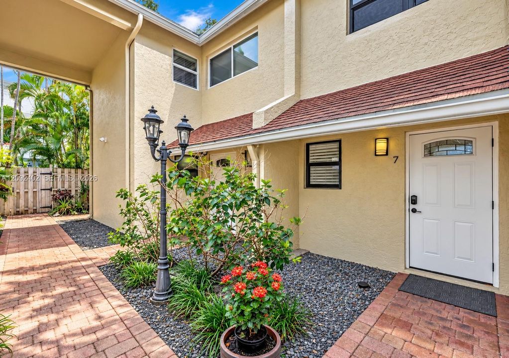 Exterior entrance featuring stucco siding, a brick paver walkway, decorative post lighting, and a front door with an arched glass insert