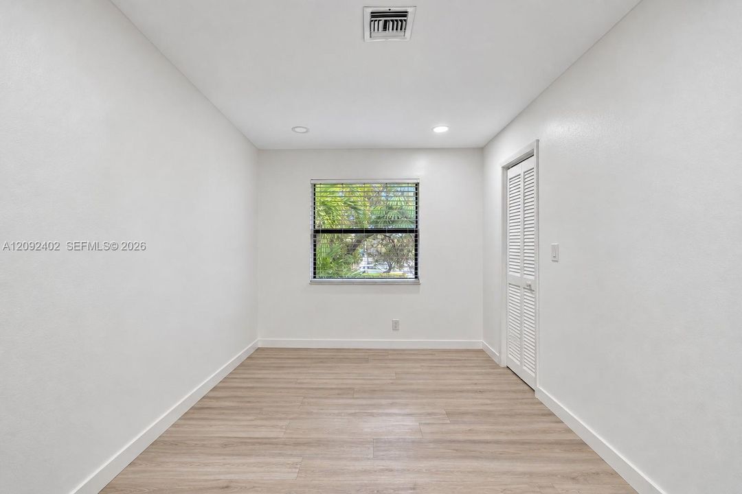 Neutral-toned room featuring wood-finish flooring, recessed lighting, and a window with horizontal blinds, complemented by a white louvered closet door