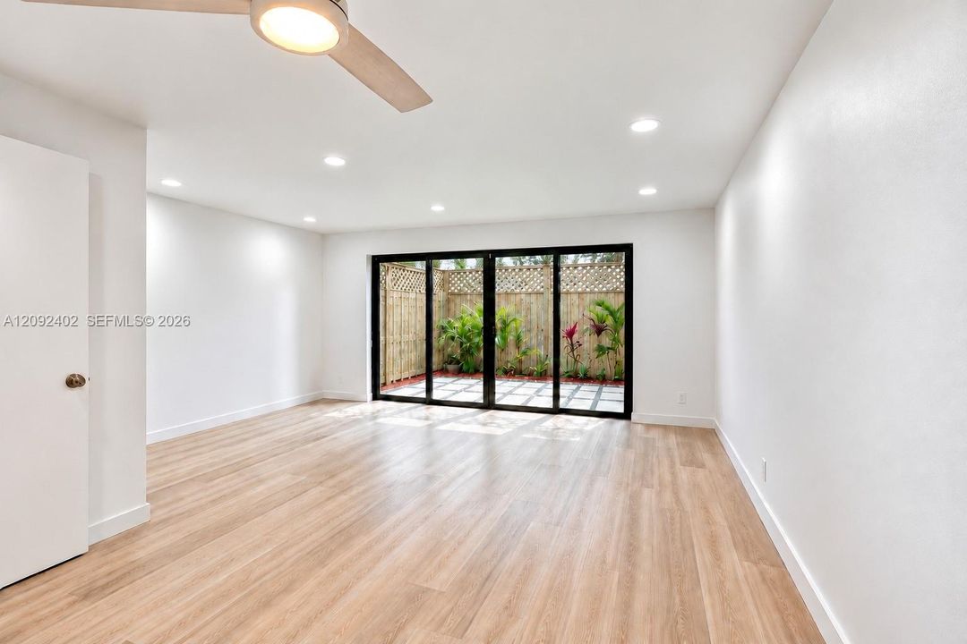 Neutral-toned interior featuring wood-finish flooring, recessed lighting, a modern ceiling fan, and black-framed multi-panel sliding glass doors opening to a fenced patio