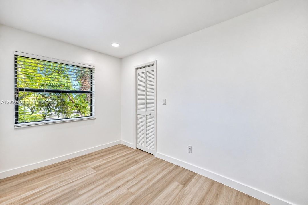 Neutral-toned room featuring wood-finish flooring, white walls, recessed ceiling lighting, and a louvered closet door