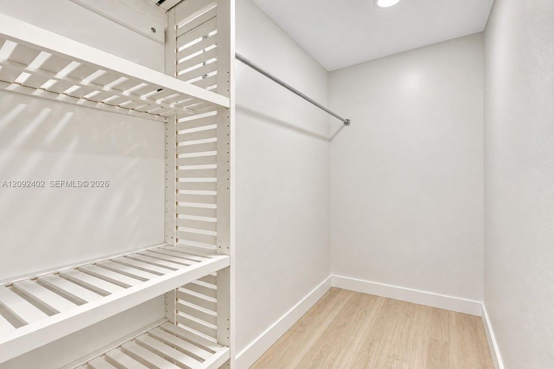Walk-in closet featuring white slatted built-in shelving, a metal hanging rod, and wood-finish flooring