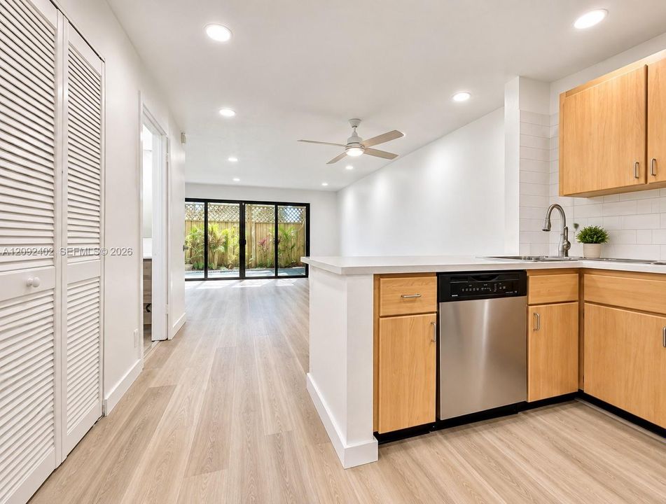 Kitchen featuring wood-finish cabinetry, stainless steel dishwasher, light-toned wood-finish flooring, recessed lighting, and floor-to-ceiling multi-panel sliding glass doors