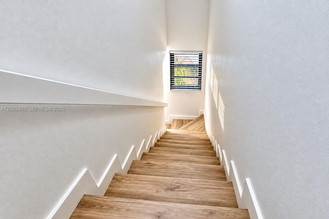 Staircase featuring wood-finish treads, white stringer detailing, a wall-mounted handrail, and a window with horizontal blinds