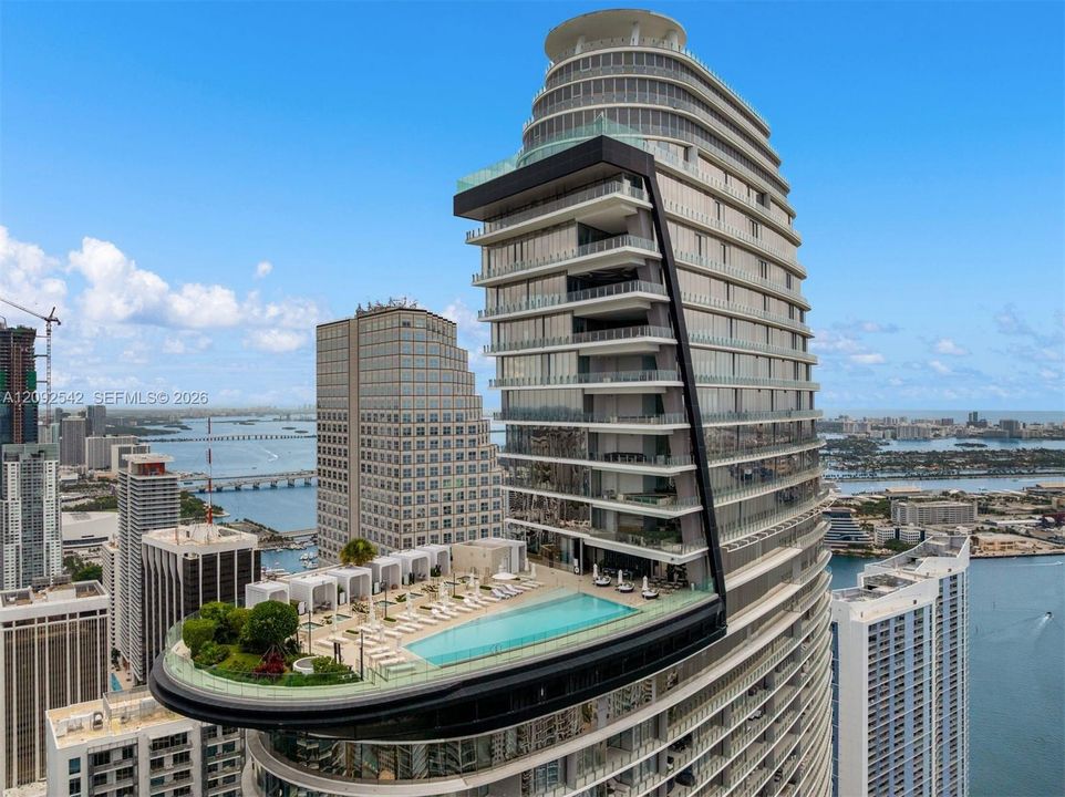 High-rise architectural structure featuring a cantilevered swimming pool, extensive wrap-around glass balcony railings, and a landscaped outdoor deck
