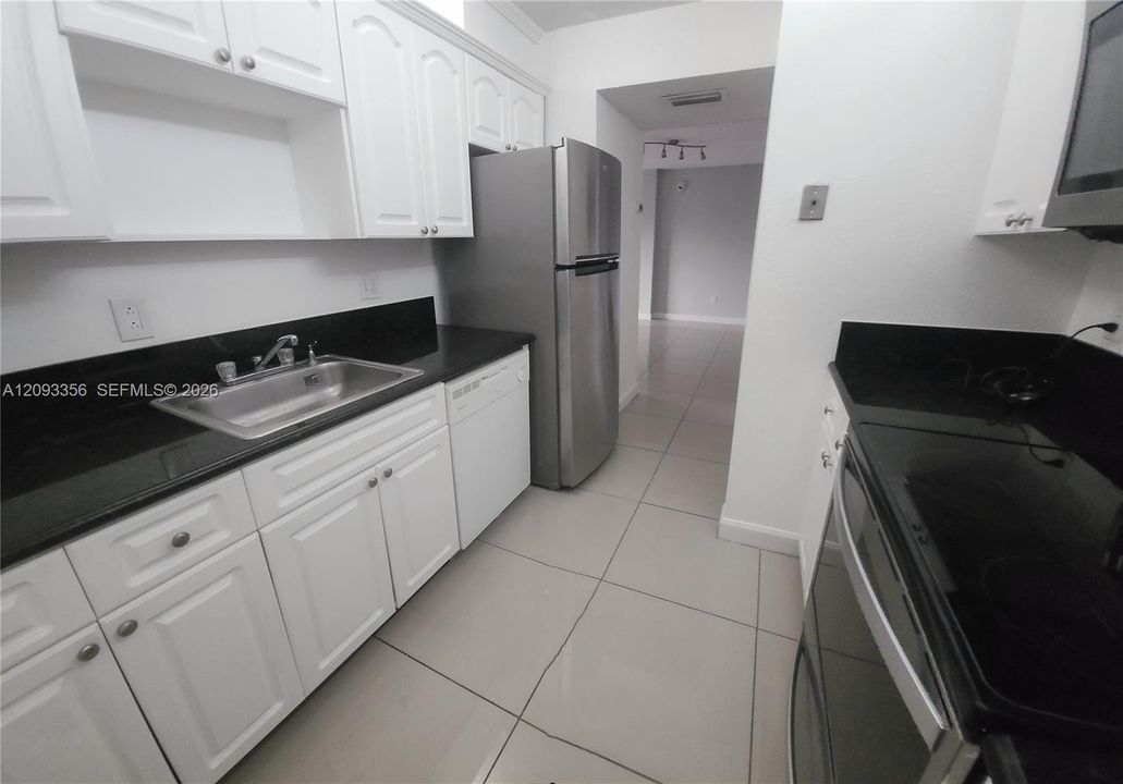 Kitchen featuring white shaker-style cabinetry, black stone countertops, stainless steel appliances, and large-format tile flooring