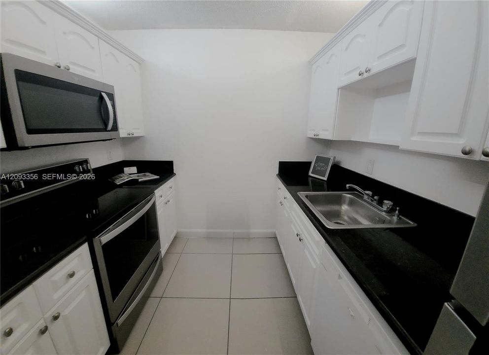 Attractive kitchen featuring white cabinetry, black quartz countertops, stainless steel appliances, and tile flooring