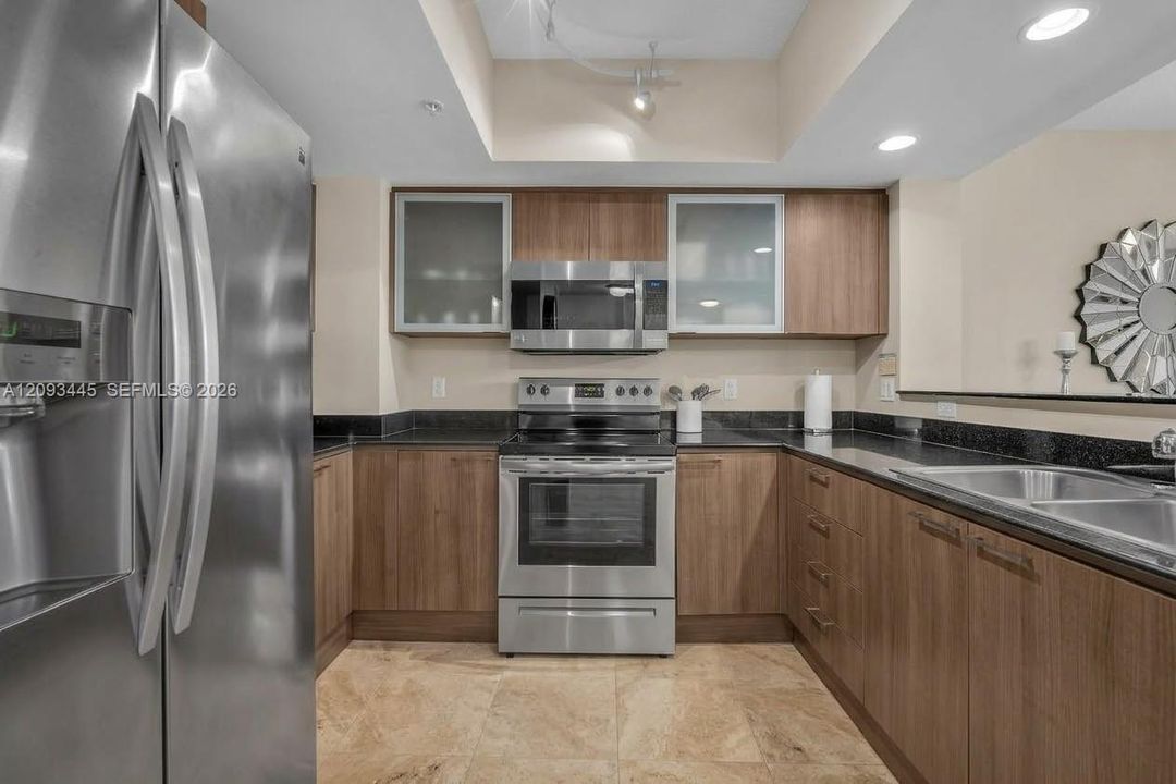 Kitchen cabinets modernized by A.I  Stainless steel appliances, wood-finish cabinetry, dark countertops, tile flooring, and recessed lighting-