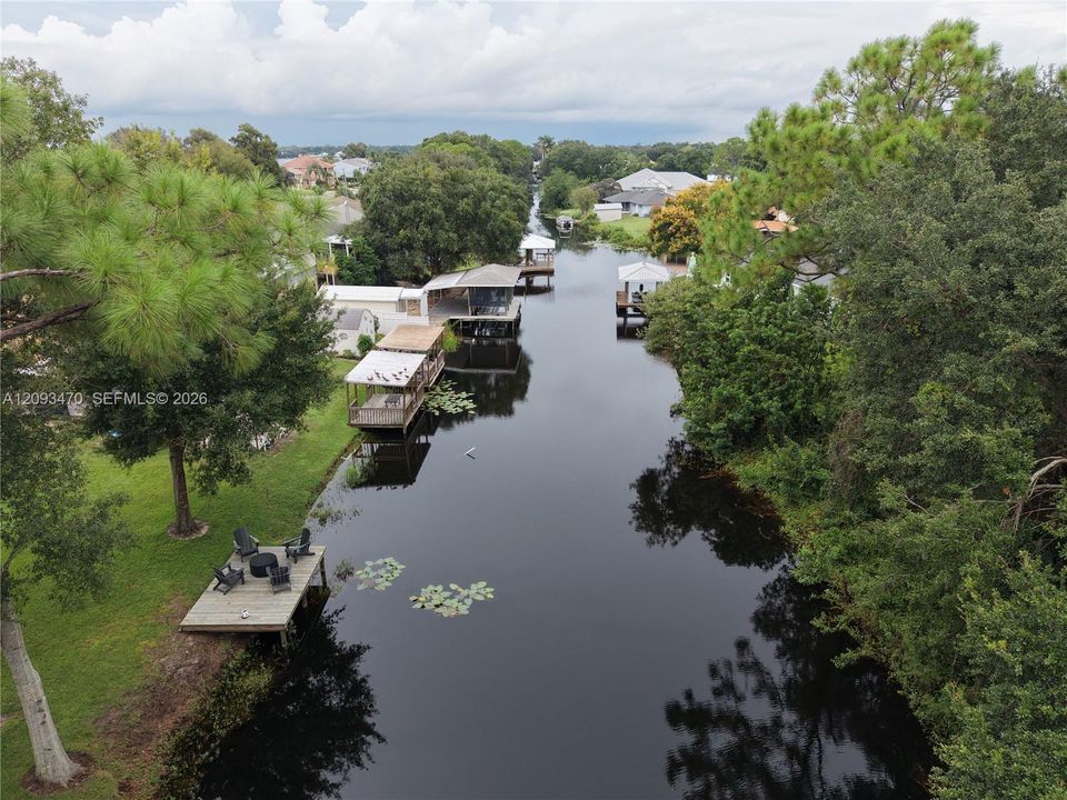 Waterfront property featuring a private wooden dock, manicured lawn, and mature trees along a canal