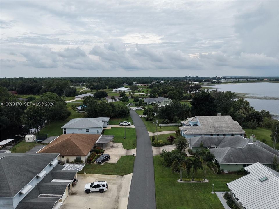 Aerial perspective of a residential neighborhood featuring asphalt roadways, manicured green lawns, mature trees, and proximity to a large body of water