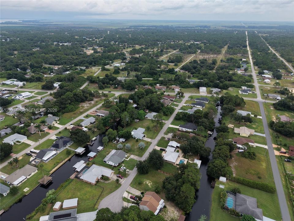 Aerial perspective of a residential neighborhood characterized by canal-front properties, mature trees, paved street grids, and open green space