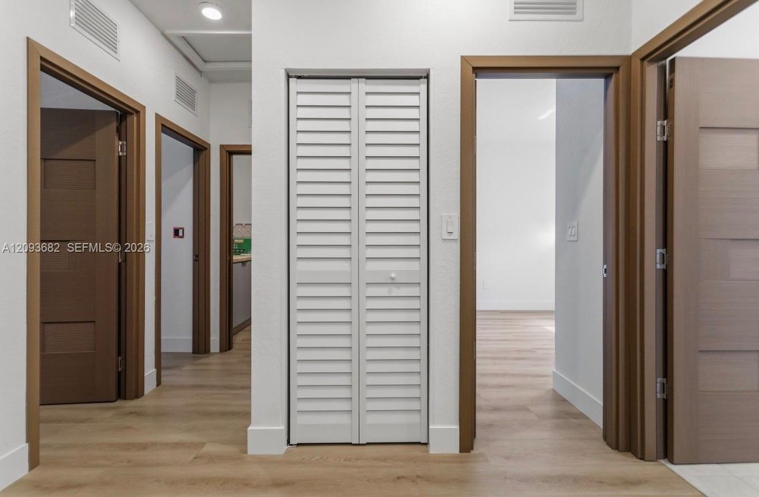 Hallway featuring wood-finish flooring, white louvered closet doors, and multi-panel interior doors with stained wood trim