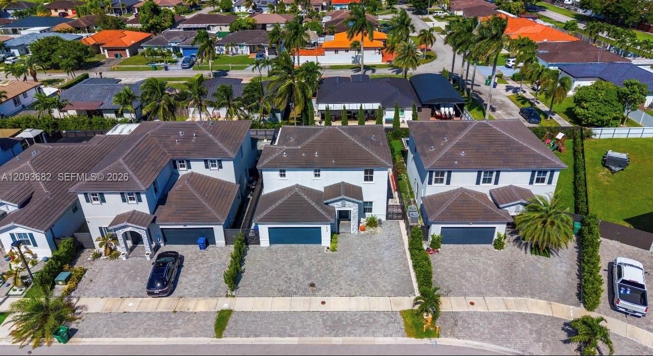 Aerial perspective featuring multi-story residences with tiled roofs, paver driveways, attached garages, and palm-accented landscaping