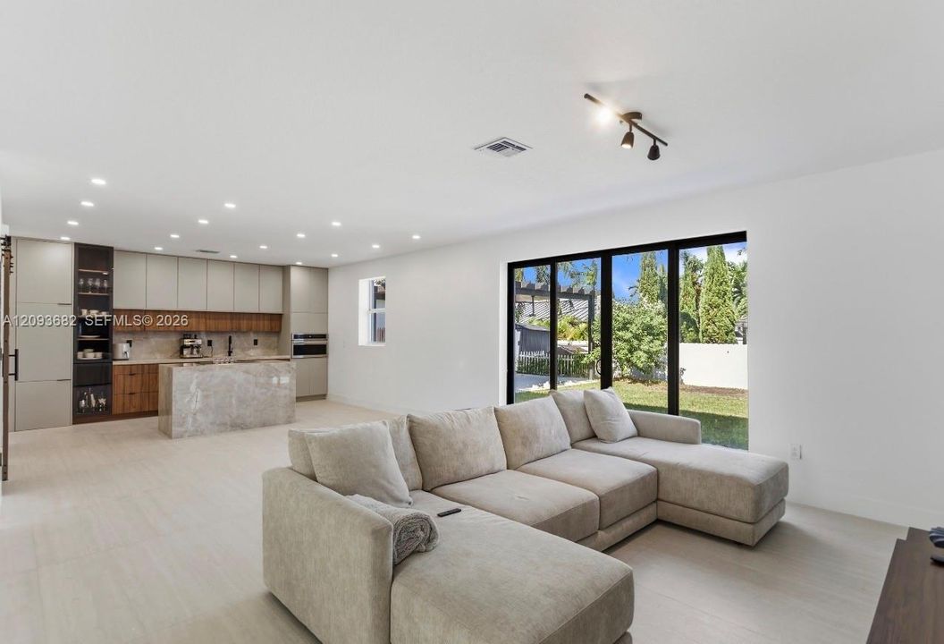 Modern kitchen featuring two-toned cabinetry, a stone-surfaced waterfall island, recessed lighting, and large-format tile flooring with multi-panel sliding glass doors