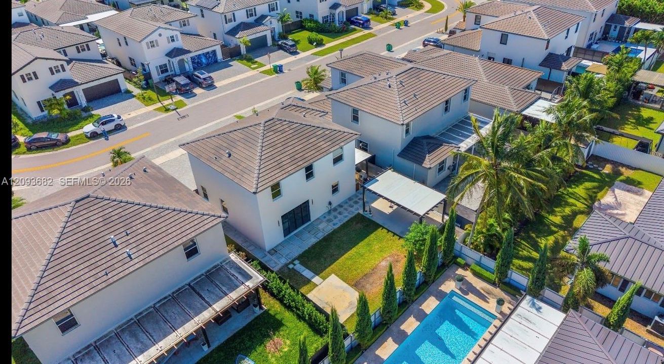 Aerial perspective of a two-story residence featuring a private swimming pool, paved patio, metal-framed pergola, and mature landscaping