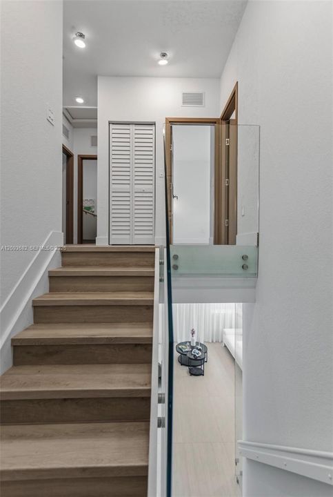 Staircase featuring wood-finish treads, glass panel railing with metallic standoffs, recessed lighting, and white louvered closet doors