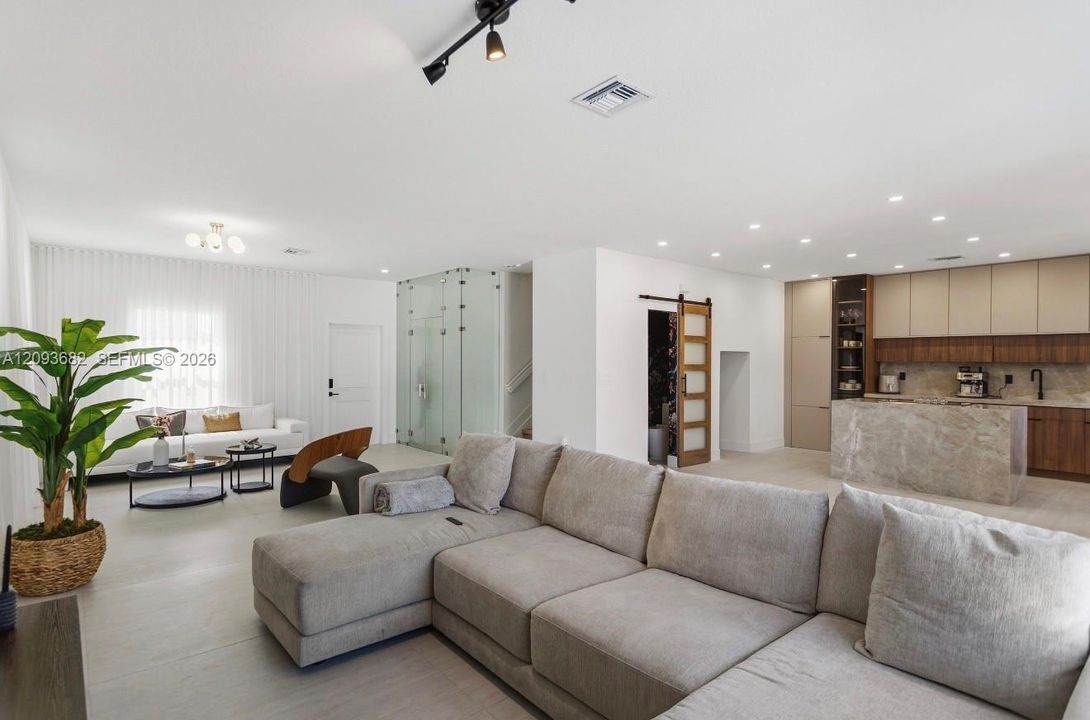 Open-concept interior featuring two-tone flat-panel cabinetry, stone-finish kitchen island, glass-enclosed feature wall, and sliding wood-and-glass barn door