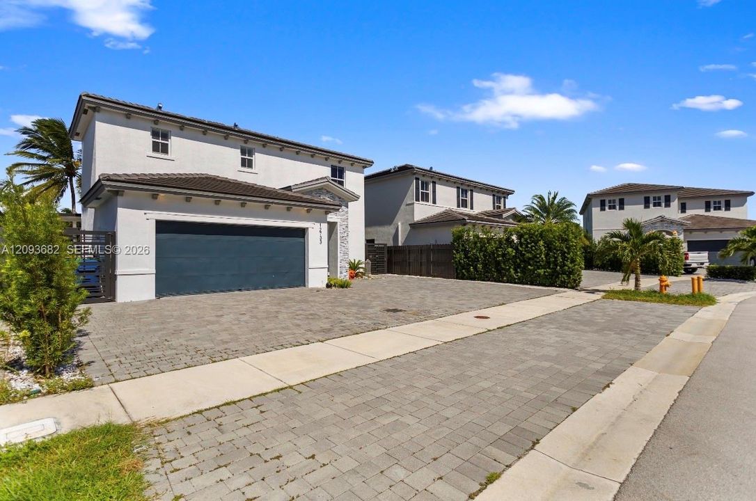 Two-story exterior featuring a light-colored stucco facade, a dark-toned multi-car garage door, and a paver driveway