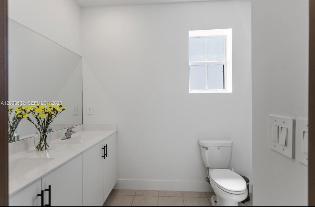 Bathroom featuring a white vanity with a composite countertop, integrated sink, large wall-mounted mirror, ceramic tile flooring, and a window