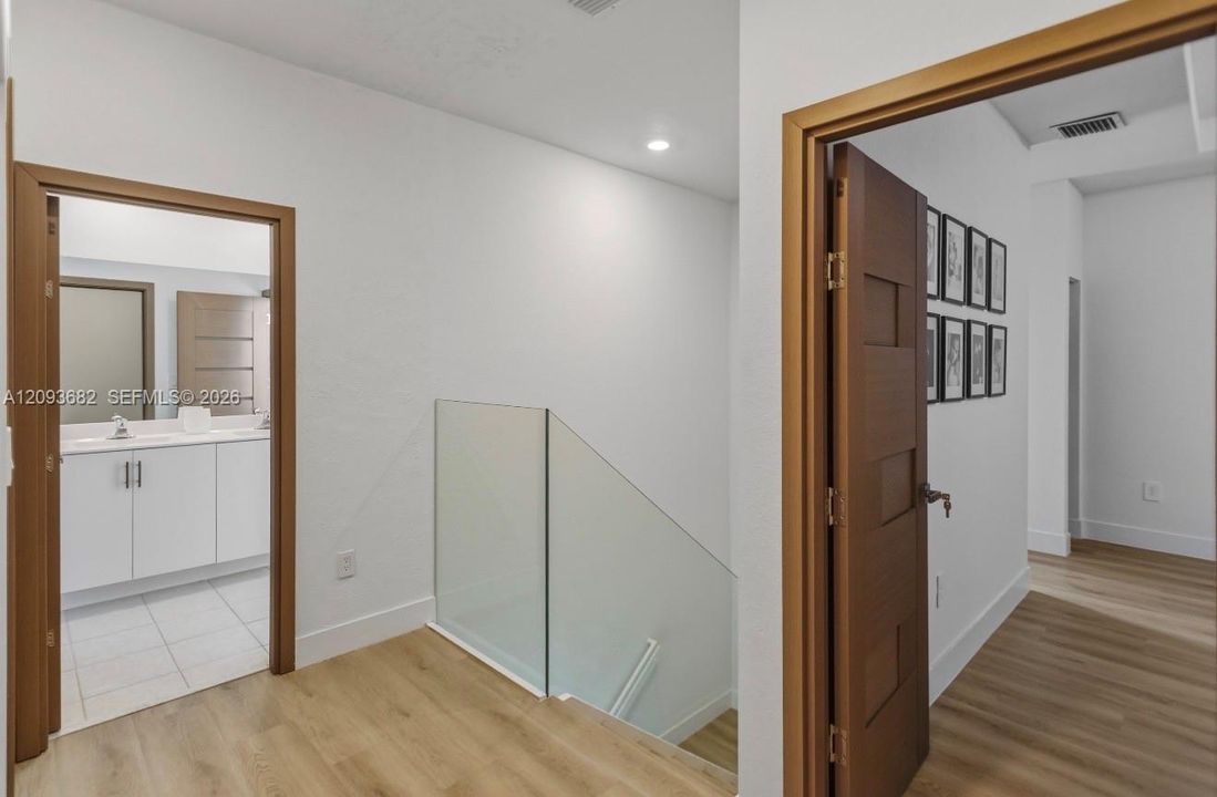 Glass panel staircase railing, wood-finish flooring, and solid core doors with horizontal paneling