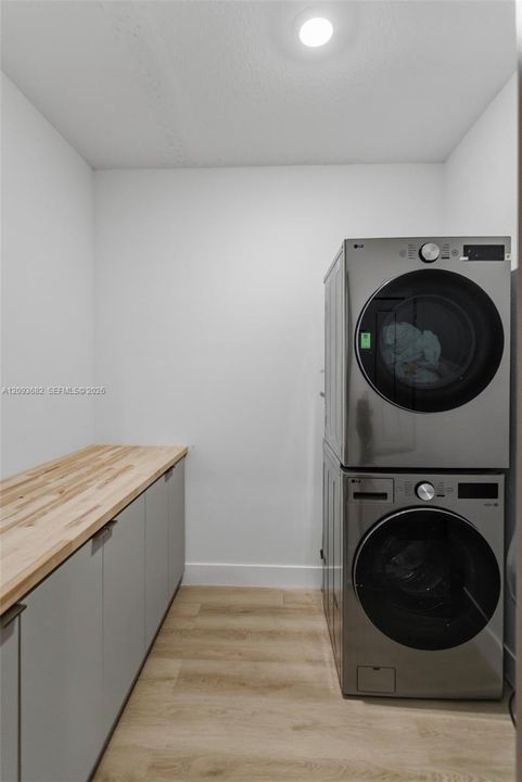 Laundry room featuring light wood-finish flooring, built-in cabinetry with a wood countertop, and recessed ceiling lighting