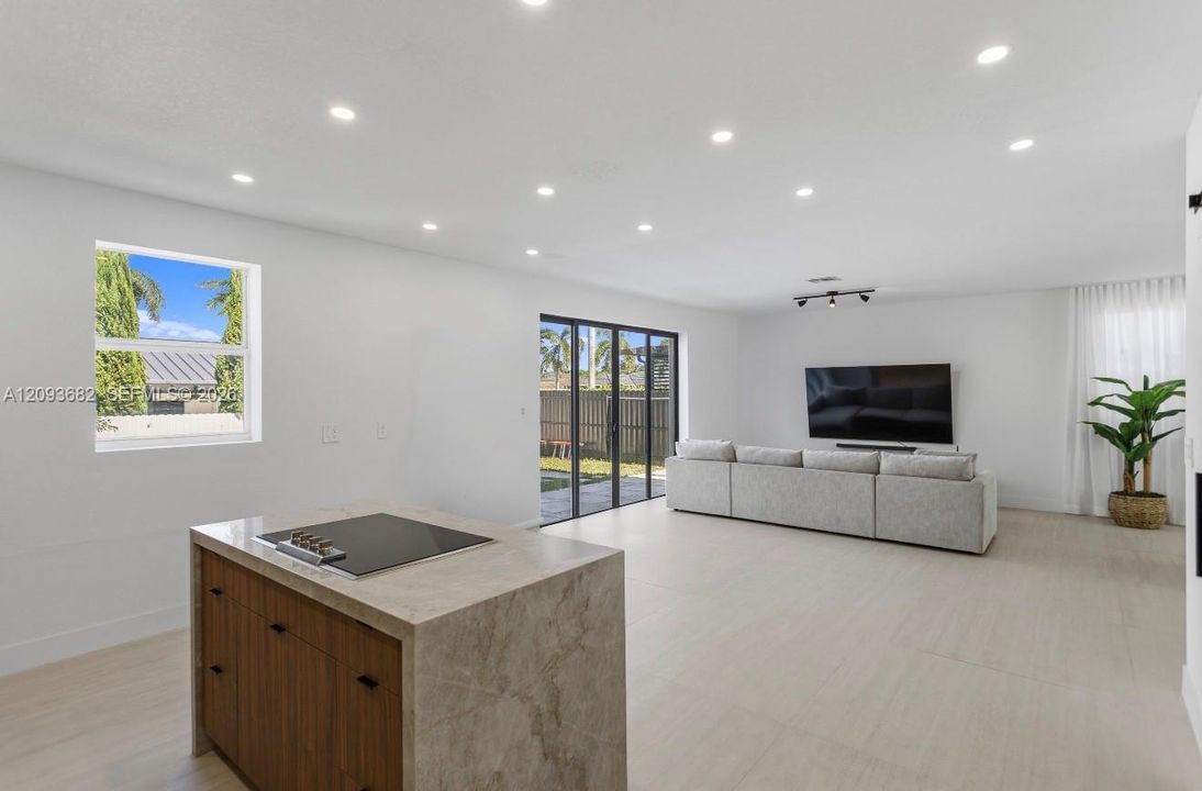 Kitchen island with a stone-surfaced countertop and integrated cooktop, complemented by recessed ceiling lighting, light-toned flooring, and floor-to-ceiling glass sliding doors