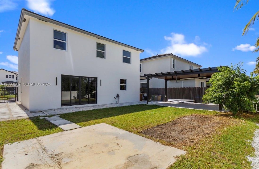 Rear exterior featuring a white stucco facade, sliding glass doors, a covered pergola, concrete hardscaping, and fenced perimeter