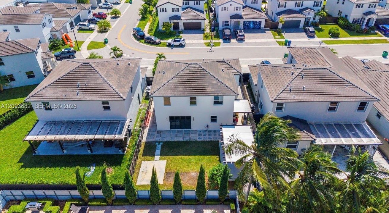 Aerial perspective featuring a two-story stucco exterior, concrete tile roof, paver patio, integrated pergola, and fenced yard