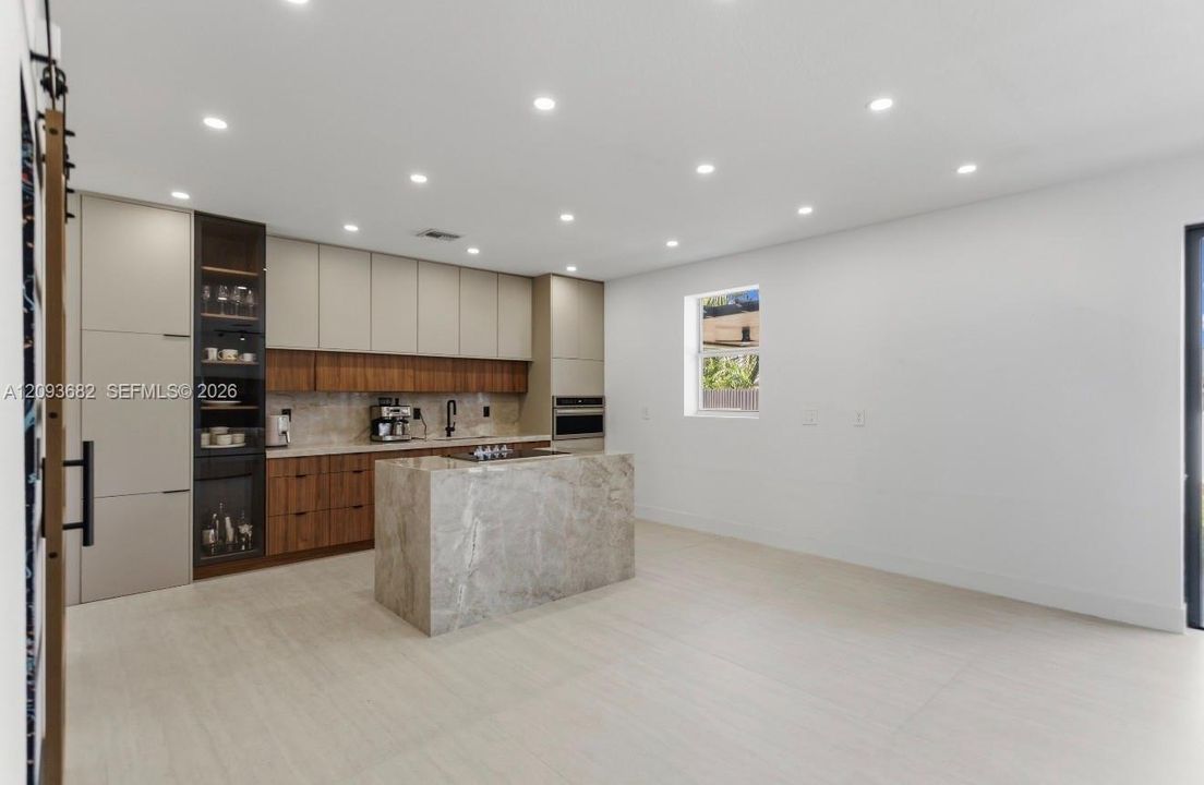 Kitchen featuring two-tone flat-panel cabinetry, a stone-surfaced waterfall island, built-in appliances, recessed lighting, and tile flooring