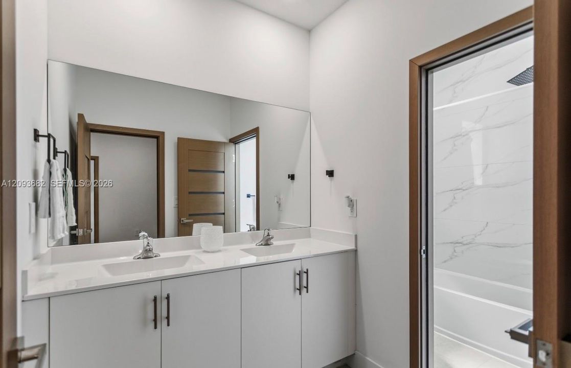 Dual vanity featuring white cabinetry, solid surface countertop, rectangular undermount sinks, and matte black hardware