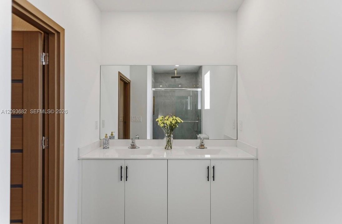 Double vanity featuring white cabinetry, a solid-surface countertop with integrated dual sinks, matte black hardware, and a full-width mirror