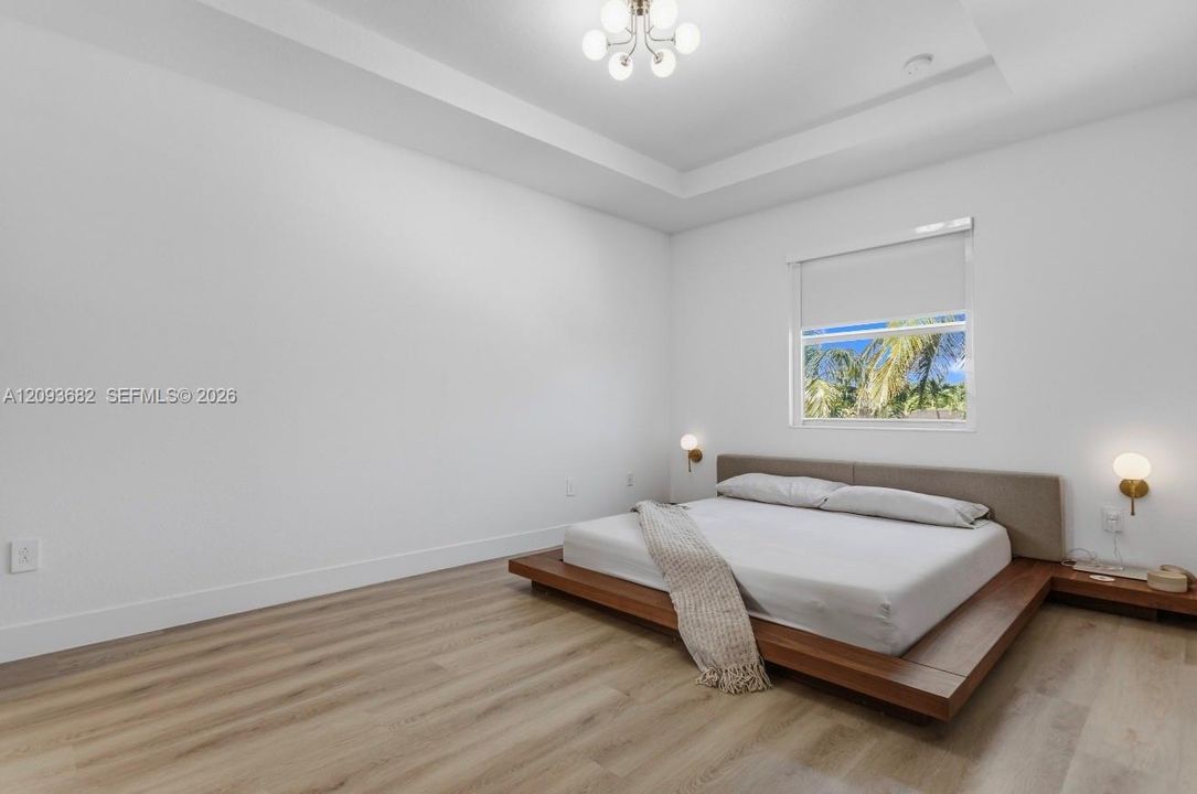 Tray ceiling, wood-finish flooring, multi-globe chandelier, and wall-mounted light fixtures