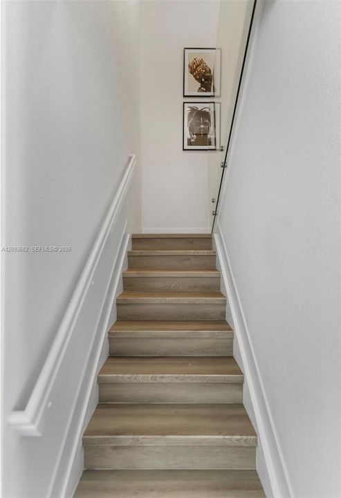 Staircase featuring wood-finish treads, a white handrail, and a structural glass railing panel