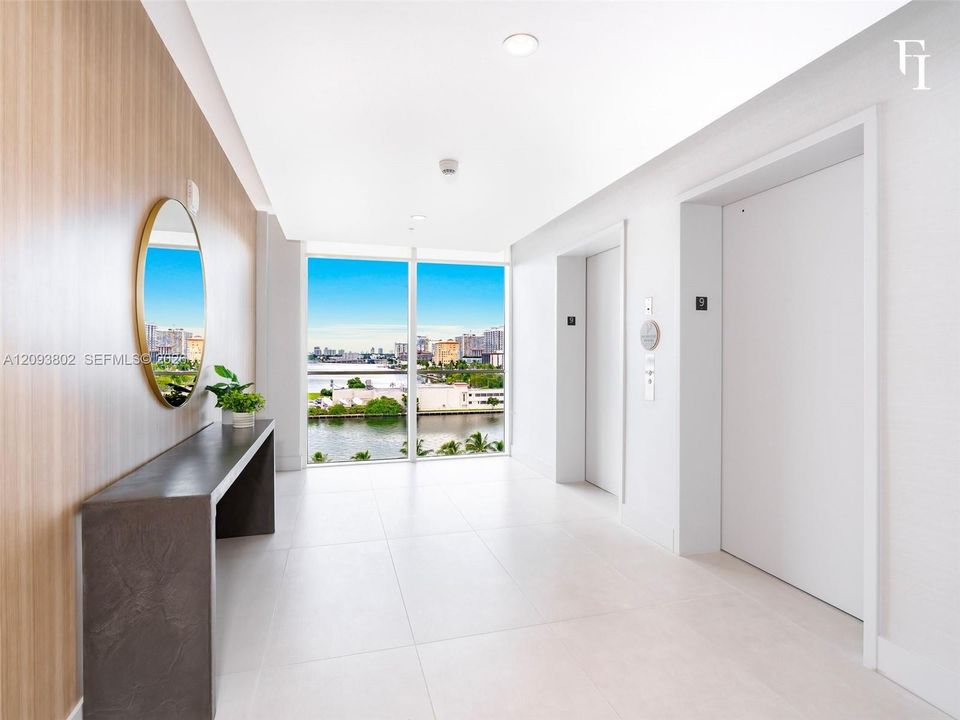 Large-format tile flooring, wood-finish wall paneling, floor-to-ceiling windows with waterfront scenery, and dual elevator access