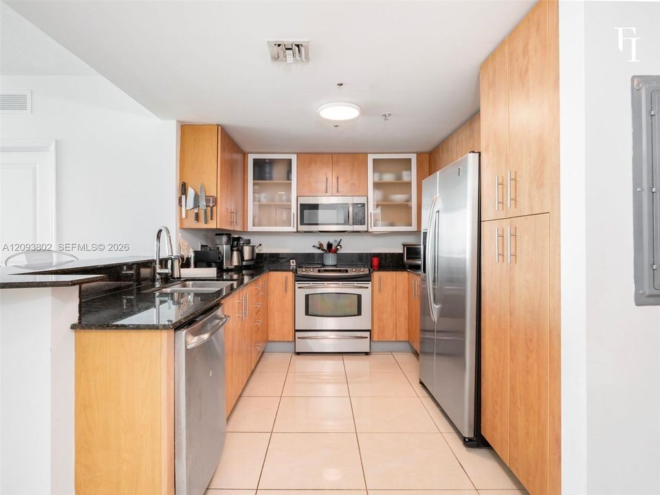 Kitchen featuring light-finish cabinetry, dark stone countertops, stainless steel appliances, glass-front upper cabinets, and tile flooring