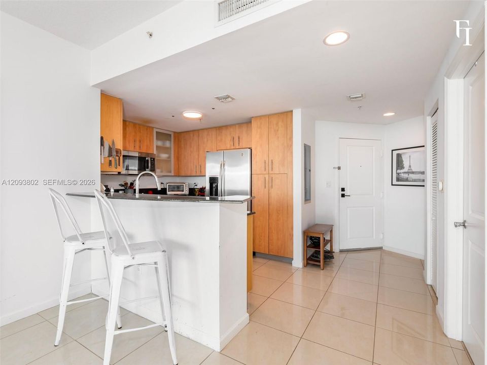 Kitchen featuring light-finish wood cabinetry, a stone-surface breakfast bar, stainless steel appliances, and tile flooring throughout