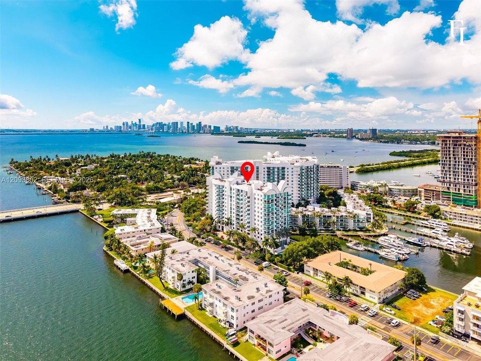 Aerial perspective of a high-rise condominium complex positioned on a waterfront peninsula, featuring direct water frontage and proximity to a marina