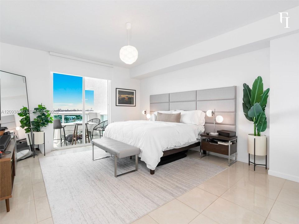 Spacious room featuring light-toned tile flooring, an oversized upholstered wall panel headboard, a modern spherical pendant light fixture, and large glass sliding doors providing external access