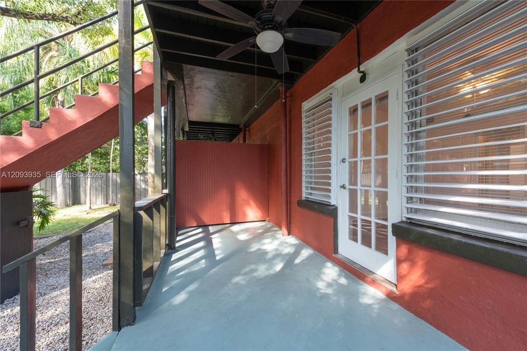 Covered outdoor patio featuring a concrete floor, integrated ceiling fan, glass-panel exterior door, and staircase with metal railings