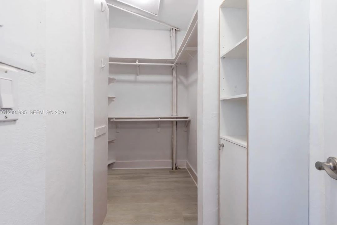 Walk-in closet featuring wood-finish flooring, multi-tier hanging rods, and built-in vertical shelving