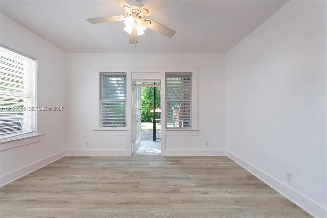 Interior space featuring wood-finish flooring, white walls, shutter-style window coverings, a ceiling-mounted light fixture with a fan, and an exterior door