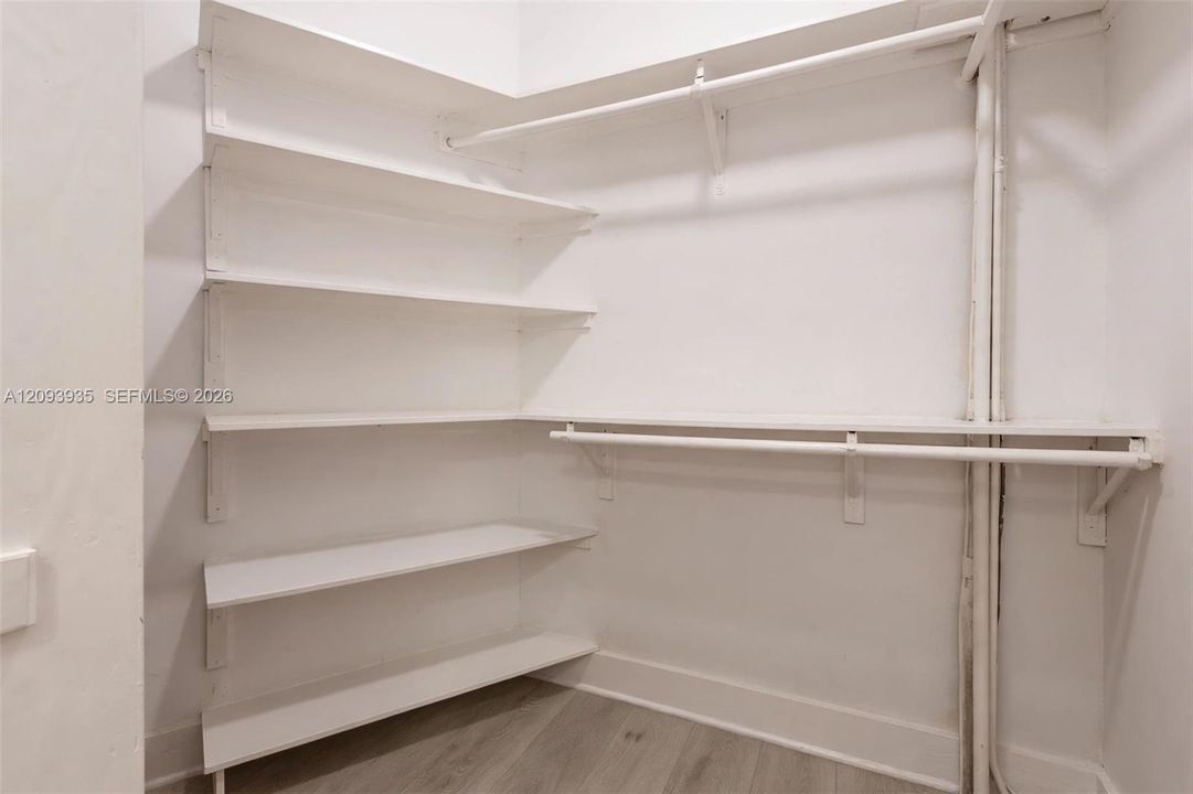 Storage area featuring white built-in shelving, dual-level hanging rods, and wood-finish flooring