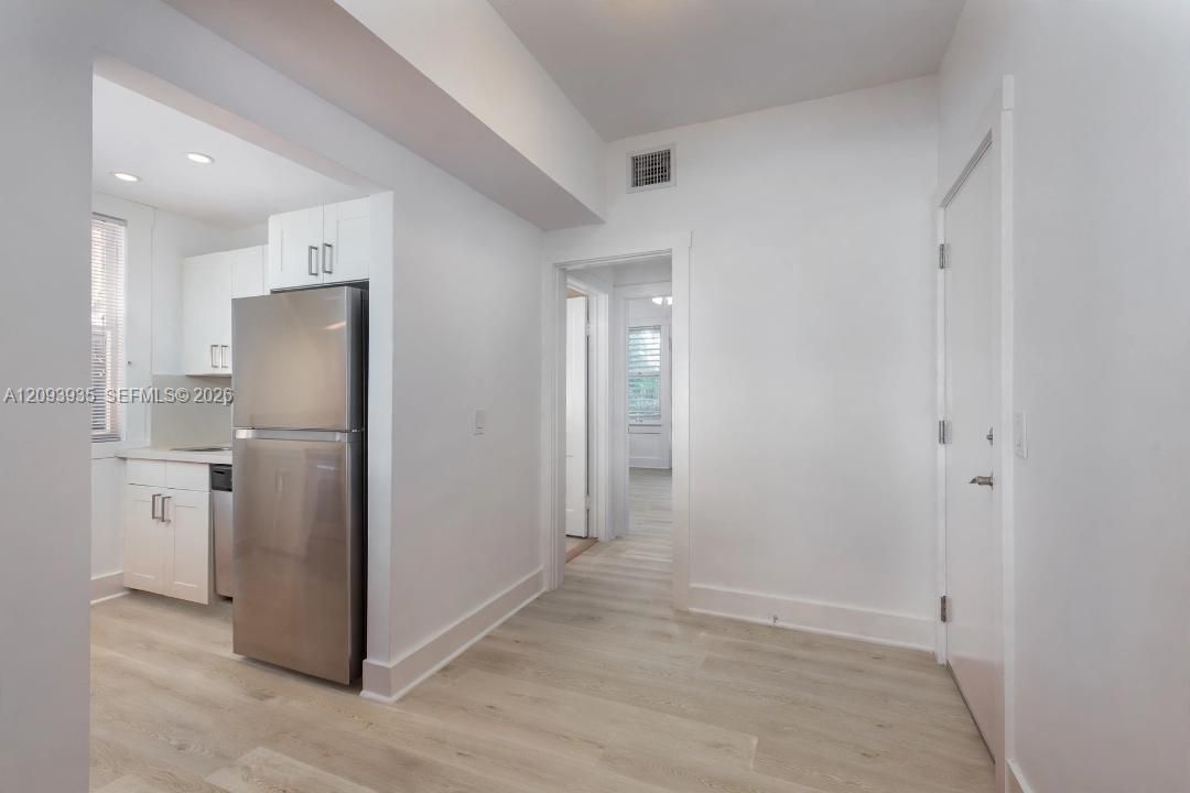 Interior featuring wood-finish flooring, white cabinetry with silver-tone hardware, and a stainless steel refrigerator