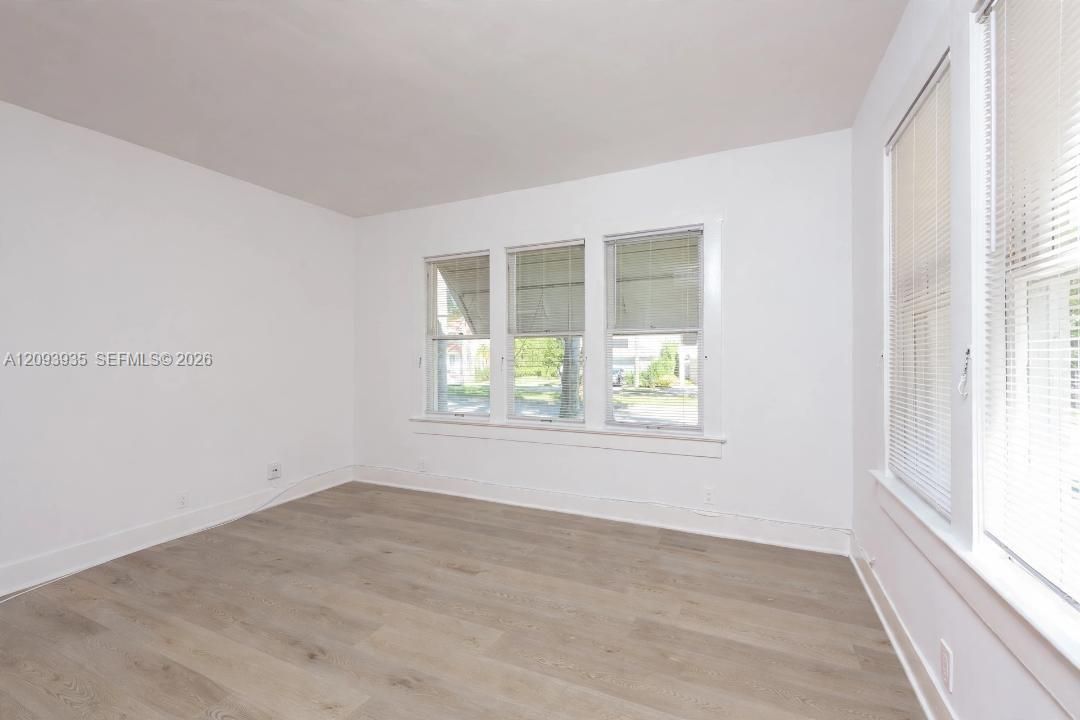 Neutral interior featuring wood-finish flooring, white walls, and multiple windows with horizontal blinds