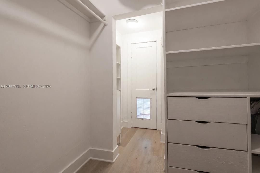 Walk-in closet featuring white built-in shelving, integrated dresser drawers, hanging rods, and wood-finish flooring