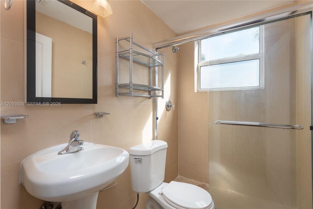 Bathroom featuring floor-to-ceiling neutral wall tile, pedestal sink, wall-mounted mirrored cabinet, glass-enclosed shower with polished chrome fixtures, and built-in metal shelving