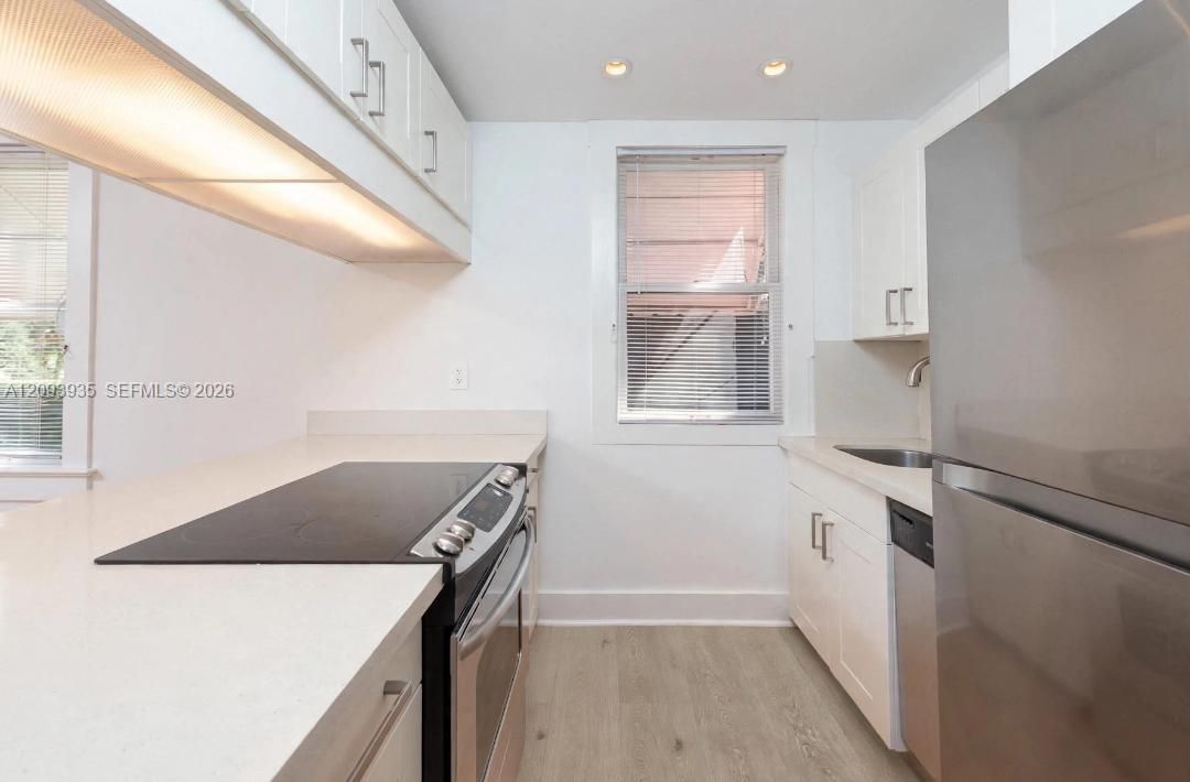 Kitchen featuring white cabinetry, solid surface countertops, stainless steel appliances, and wood-finish flooring