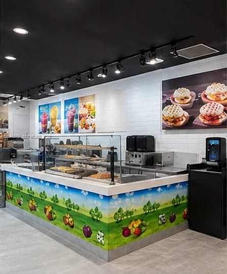 Service counter with a glass partition, white tile wall finish, track lighting, and neutral-tone flooring