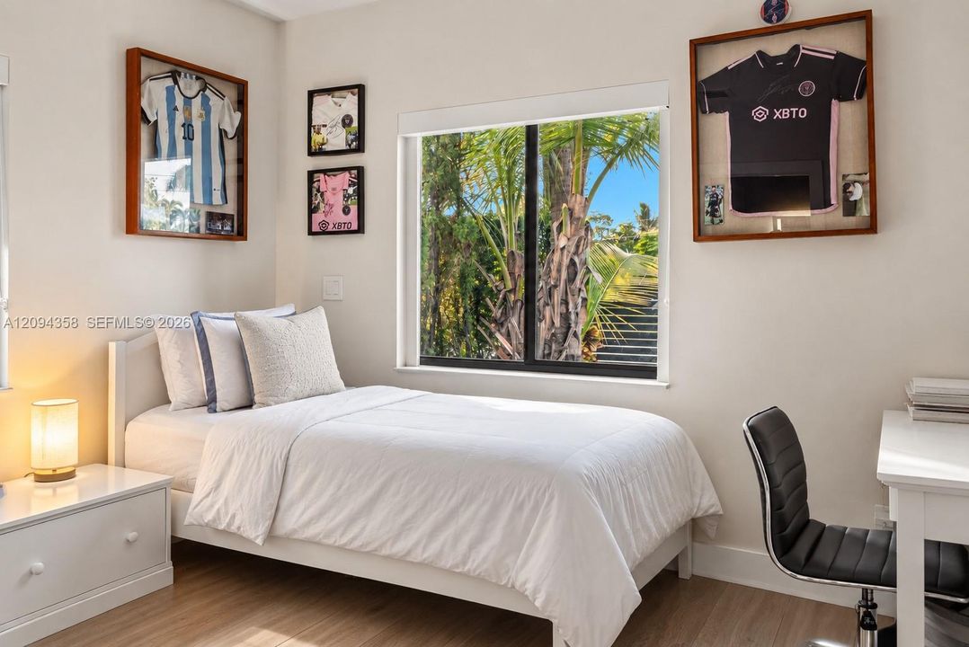 Room featuring light wood-finish flooring, neutral wall tones, and a large window with exterior palm tree scenery