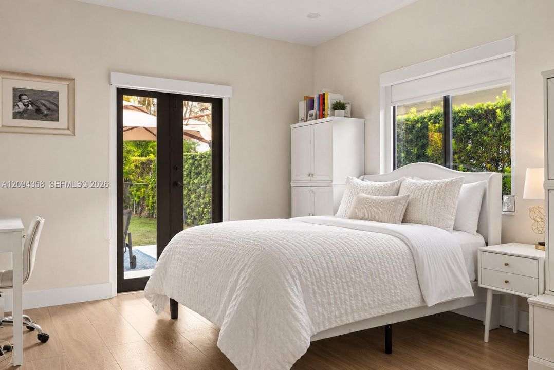 Light-filled room featuring wood-finish flooring, a white built-in storage cabinet, and black-framed French doors opening to an outdoor area